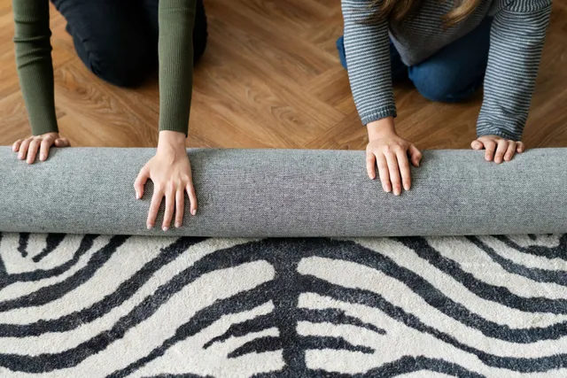 Two people are rolling a rug on the floor.