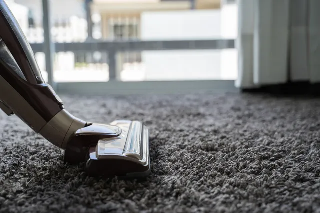 A vacuum cleaner is cleaning a carpet in a living room.