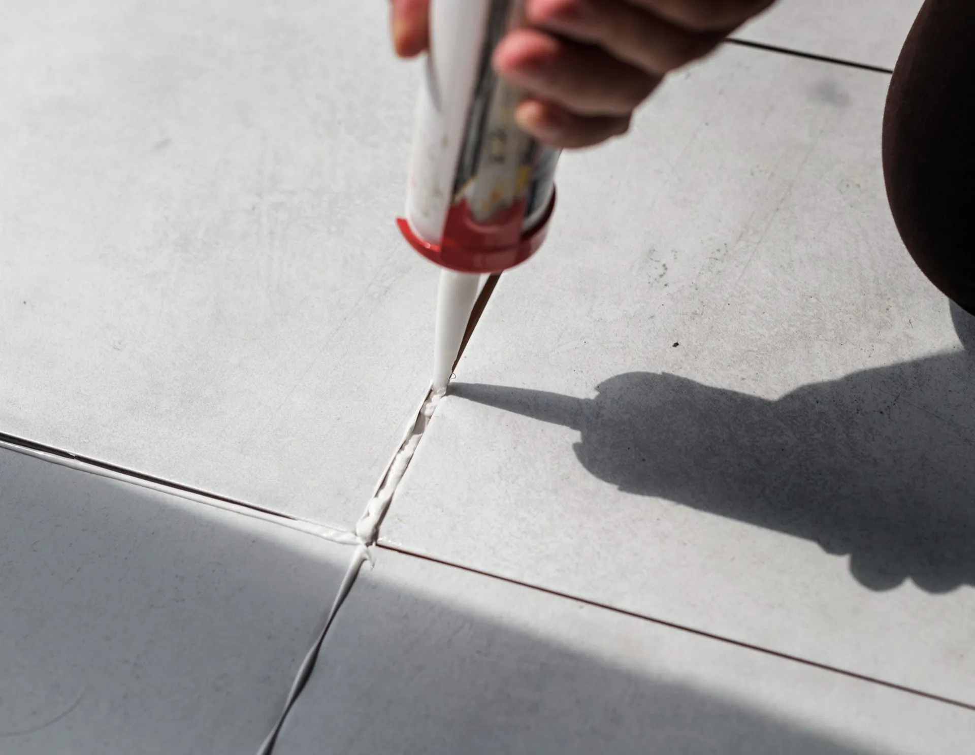 A person is applying a sealant to a tile floor.