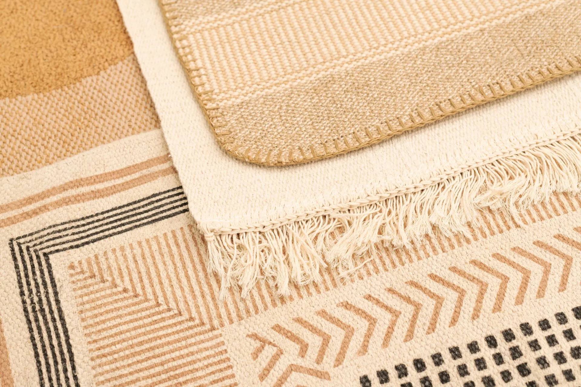 Close-up of three beige and tan rugs with geometric patterns.