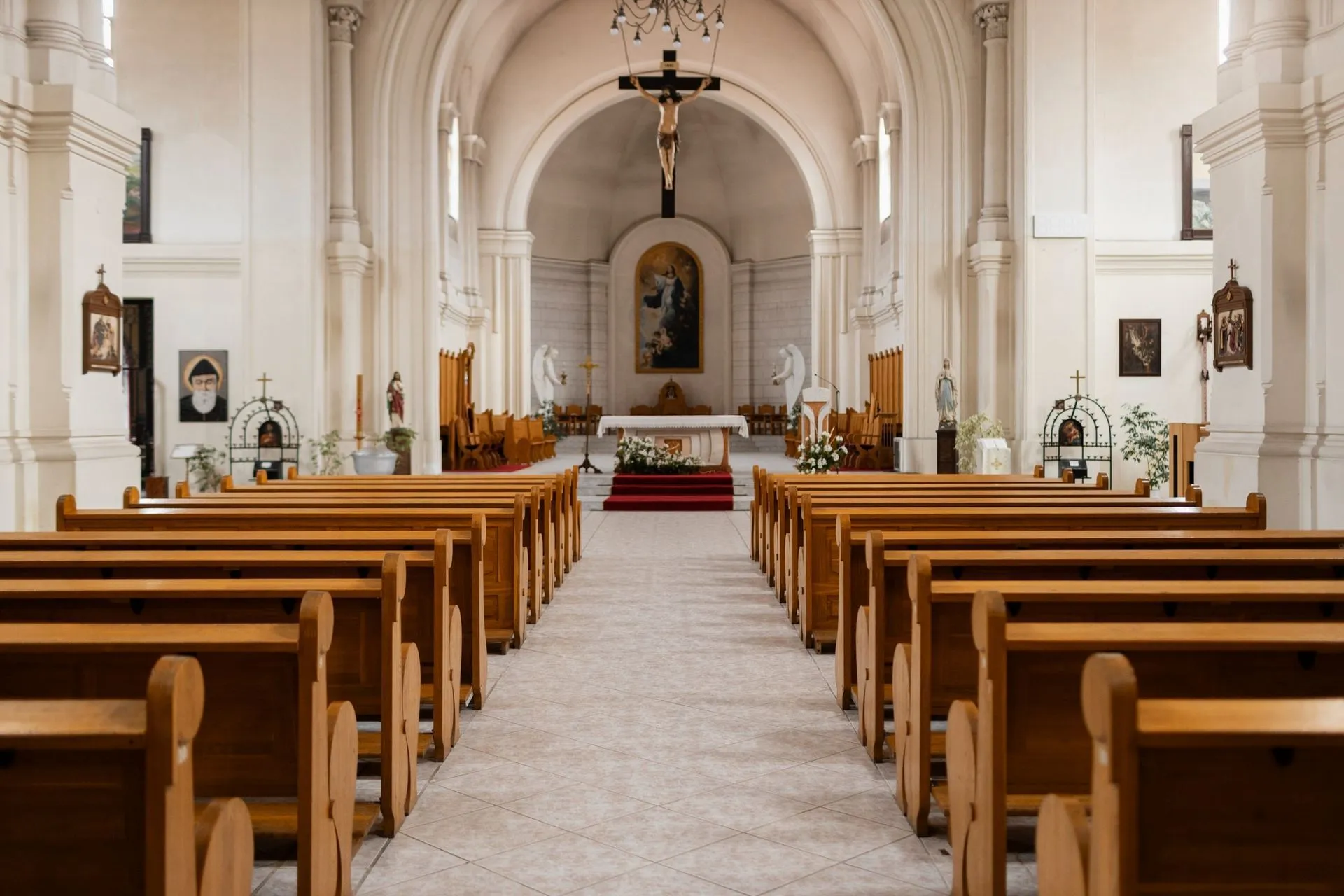 The inside of an empty church with wooden benches and a cross on the altar.