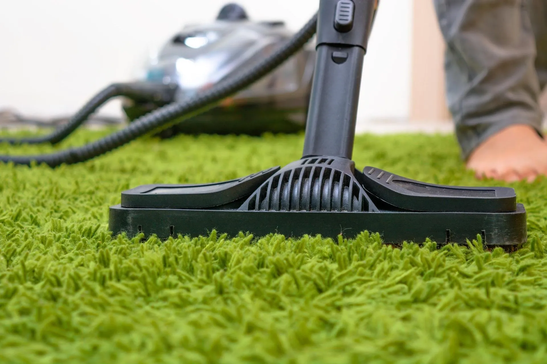 A person in Carpet Cleaning Company Vancouver uses a vacuum cleaner to clean a green carpet.