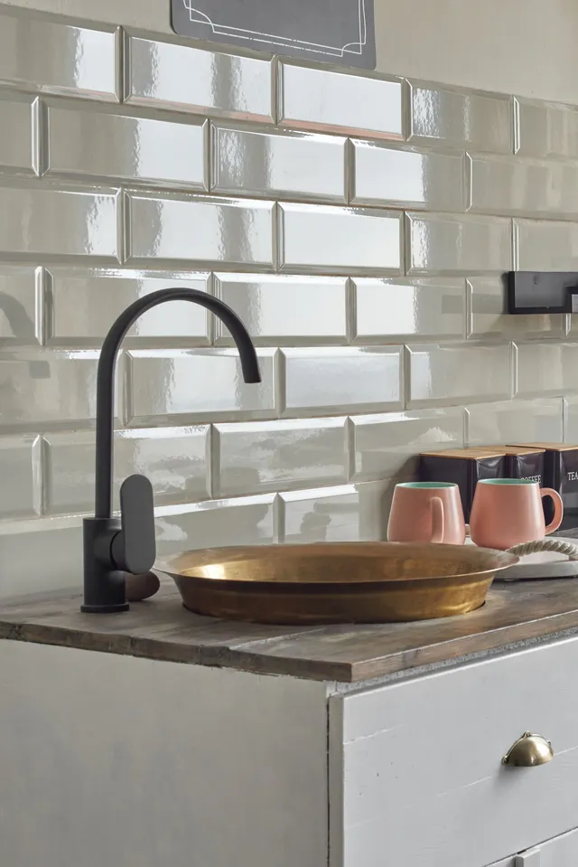 Black faucet over a gold basin set into a wooden counter, against white subway tile backsplash.