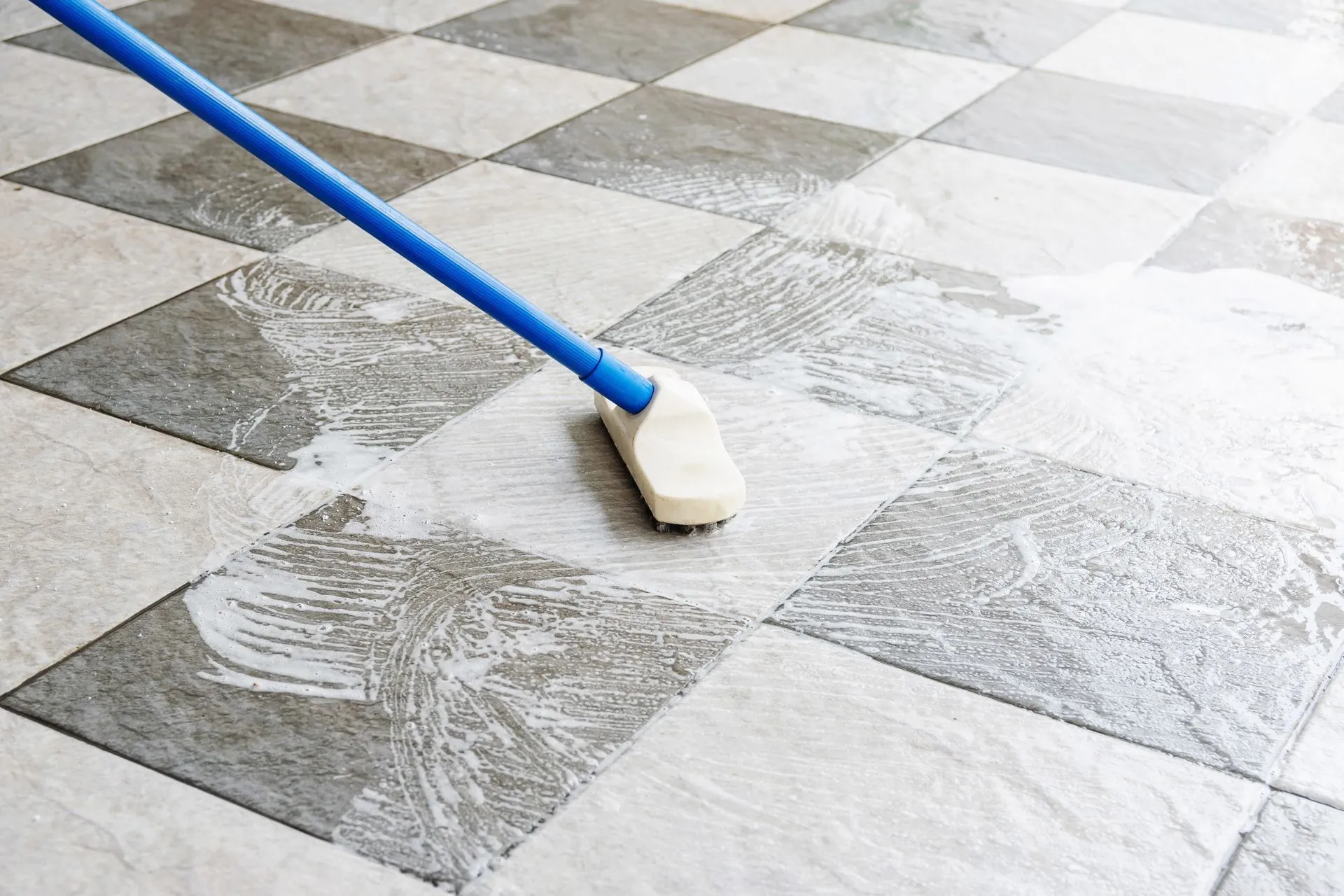 A person is cleaning a checkered tile floor with a mop.