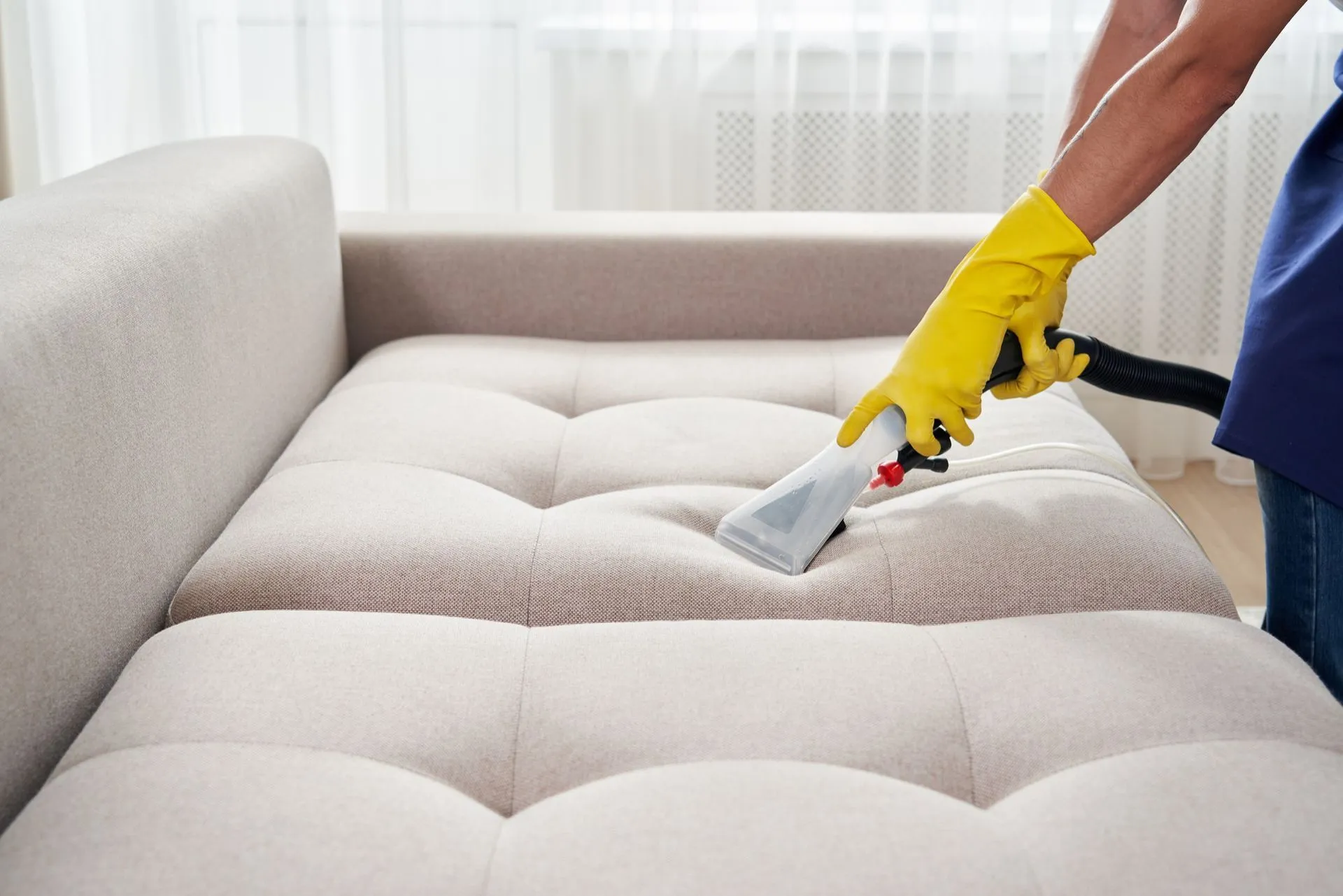A person is cleaning a couch with a vacuum cleaner.